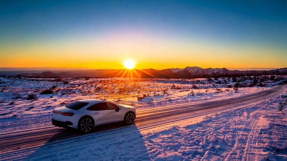 car driving into  sunset in snowy mountain valley