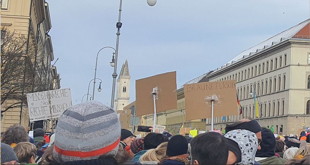 Menschenrechte statt rechte Menschen steht auf einem Plakat, viele Leute auf Demo, im Hintergrund die Ludwigskirche in München