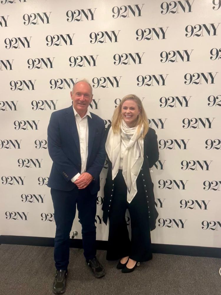 Tim stood next to Camille smiling with a background with the 92NY lettering appearing multiple times. 