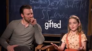 A snap from a video promoting the movie Gifted. Star Chris Evans on the left, star McKenna Grace on the right. They sit in chairs in front of a blackboard with a complex mathematical equation from the movie.