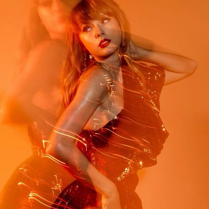 Taylor Swift against an orange background, she’s posing looking to the left with one hand behind her head and the photo is blurred 