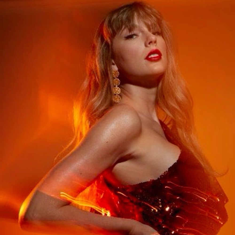 Taylor Swift against an orange background with her hand on her hip looking into the camera 