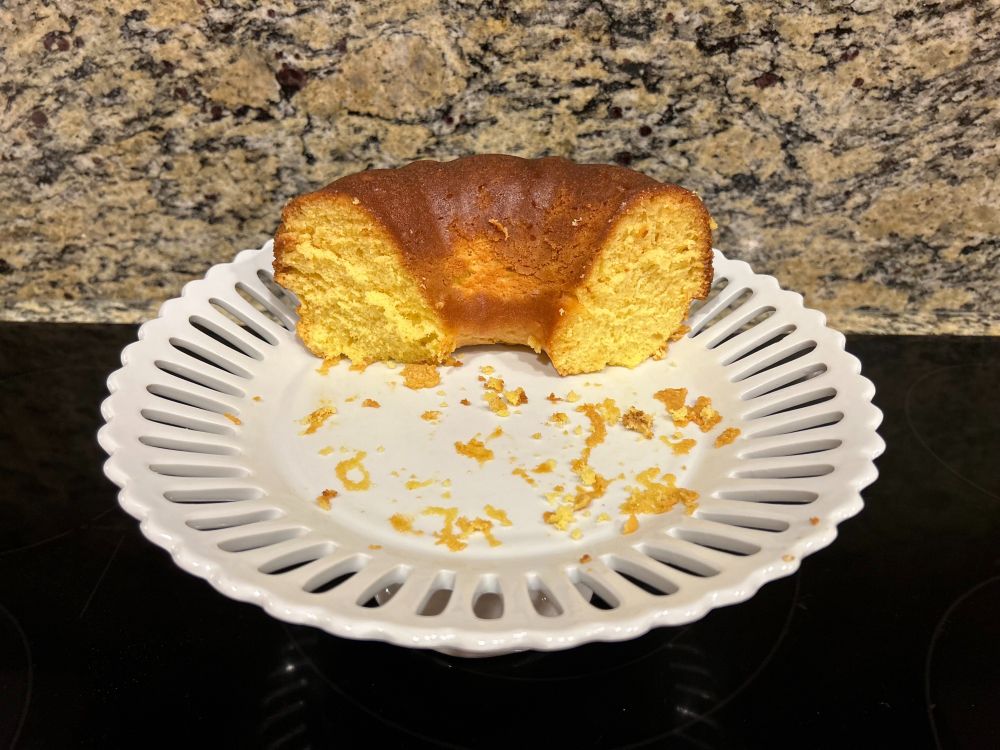 1/3 of an orange bundt cake on a white cake pedestal with crumbs sticking to the plate