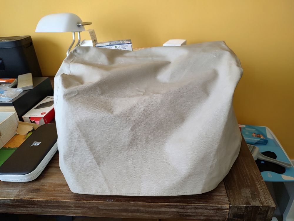A beige cover for a typewriter covering a typewriter. It sits on a dark brown desk.