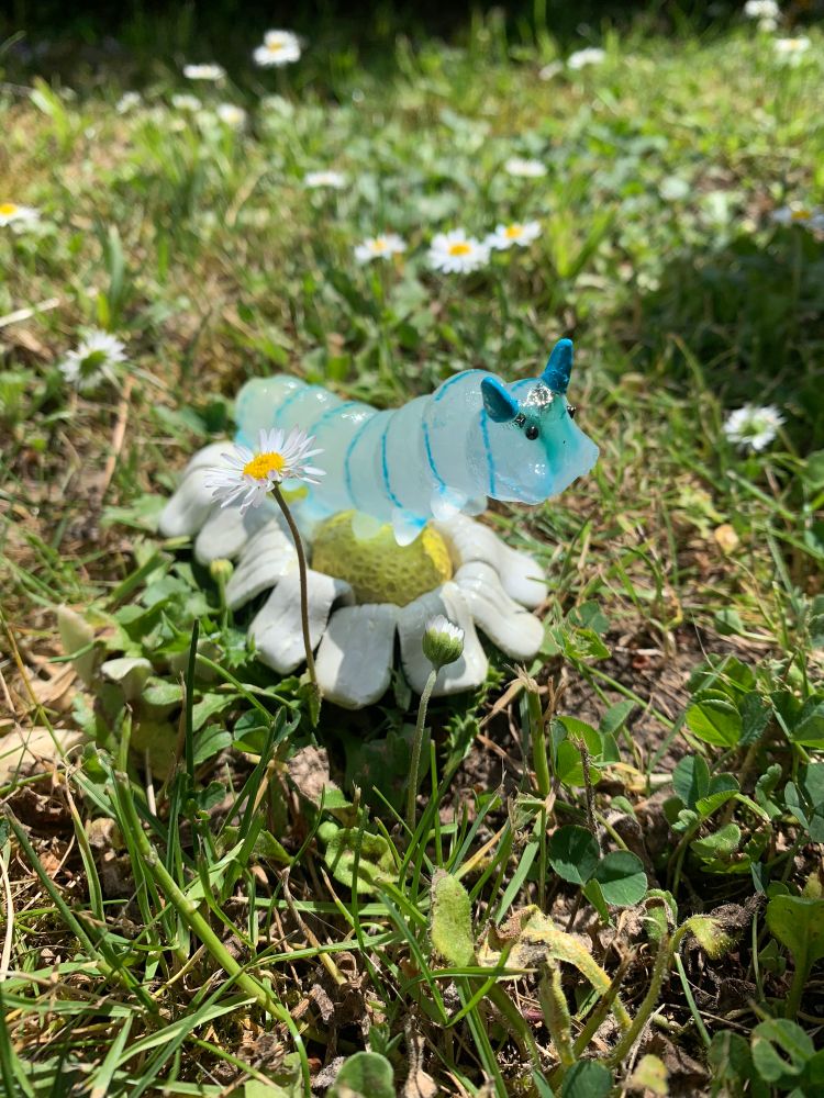 Photo d’une chenille en verre sur des pâquerette en argile epoxy qui est posée sur l’herbe