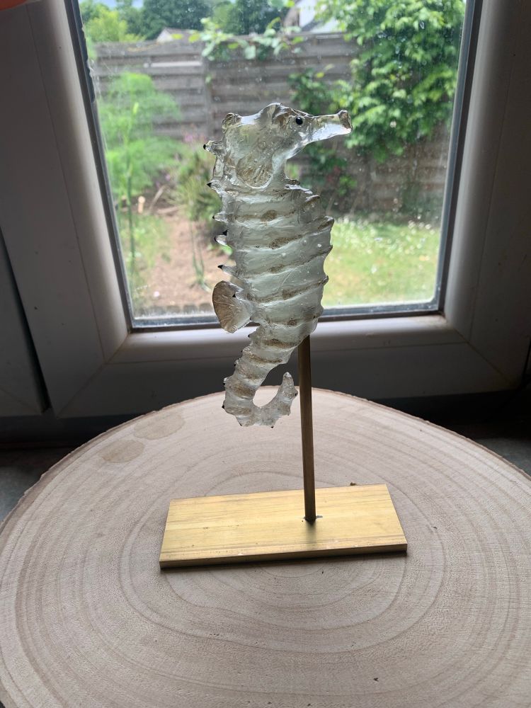 Photo d’une sculpture d’hippocampe en verre sur un socle dorée en laiton 