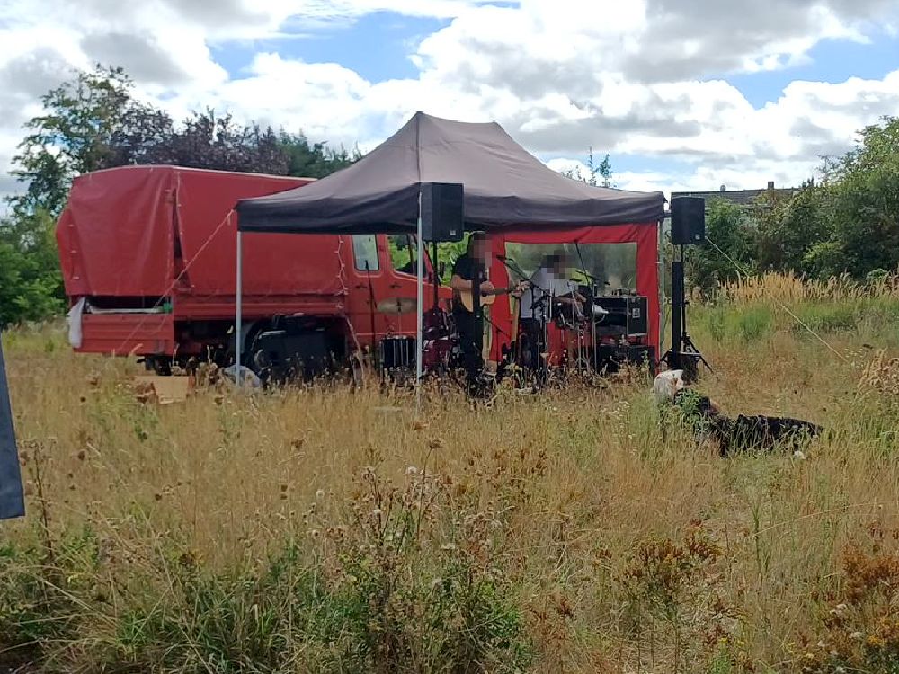 ein roter Pavillon steht vor einem roten LKW auf einer Wiese, darunter spielt eine Band