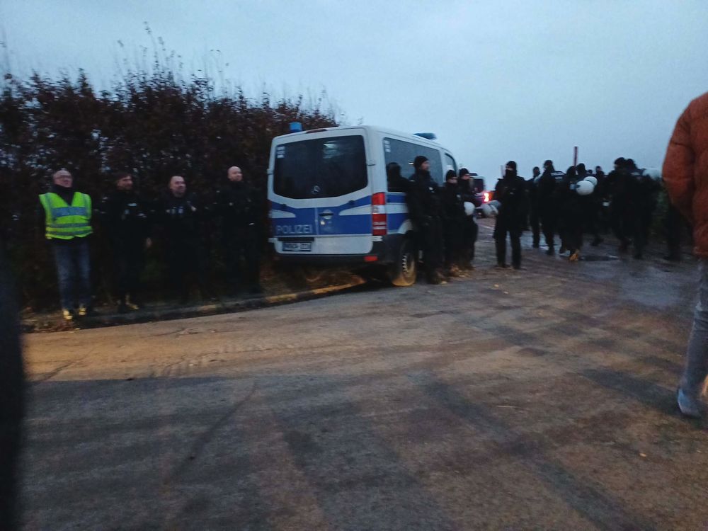 Eine Polizeikette mit Transporter steht vor einer Hecke.