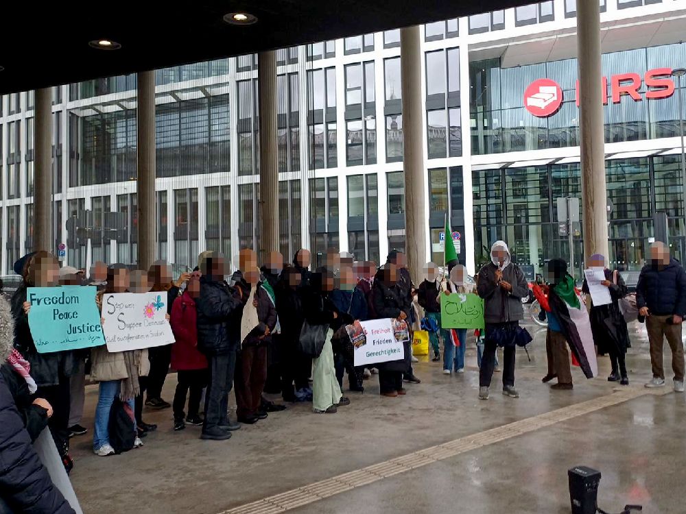 Unter dem U-Bahn-Vordach am Breslauer Platz stehen Dutzende Demonstrant*innen mit Pappschildern und fordern Freiheit, Frieden und Gerechtigkeit für die Zivilbevölkerung im Sudan 
