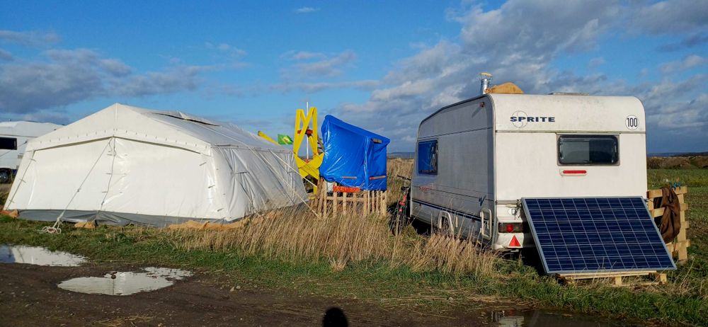Neue Mahnwache auf der Wiese des BUND an der Tagebaukante, bestehend aus einem Wohnwagen mit Solarzelle, einem Kompostklo, einem weißen Gemeinschaftszelt und einem großen Widerstands-X im Hintergrund