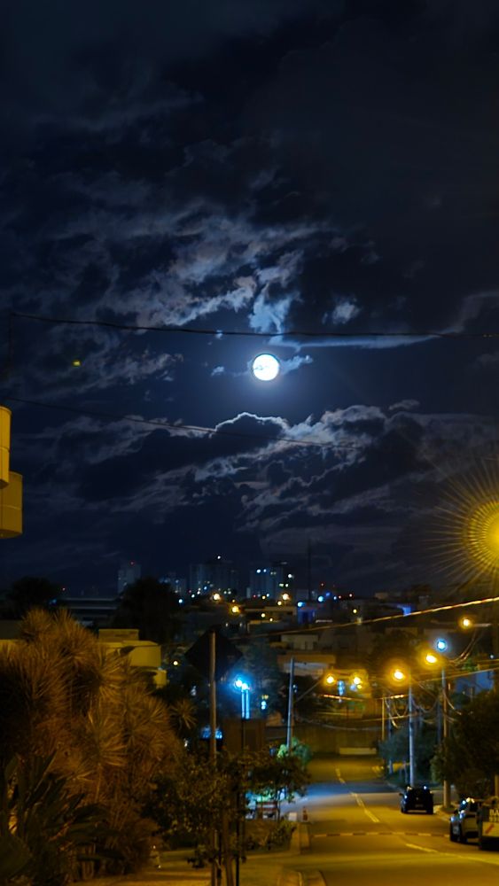 lua cheia em meio a nuvens iluminando uma rua 