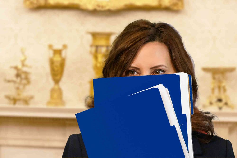 Gov. Whitmer in the Oval Office holding blue folder in front of her face.