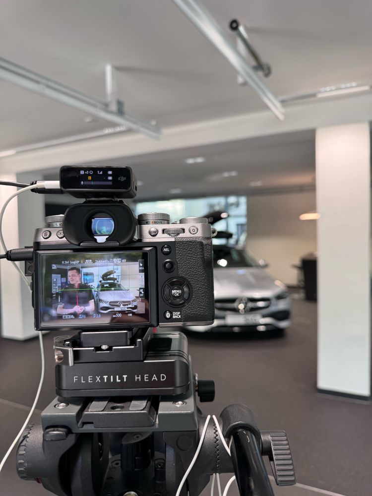 Im Vordergrund steht eine Kamera, im Hintergrund sieht man einen Mercedes