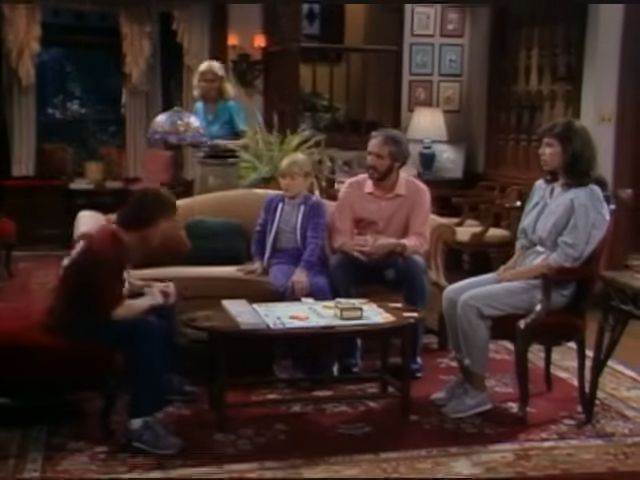 Still from the TV show Family Ties, with a family playing a board game. The home around it has an eclectic decor.