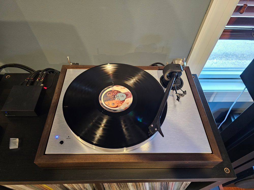 A turntable playing Cosmic Kraut Jam by Trigon. The record is on black vinyl with custom labels showing the 3-faced being.