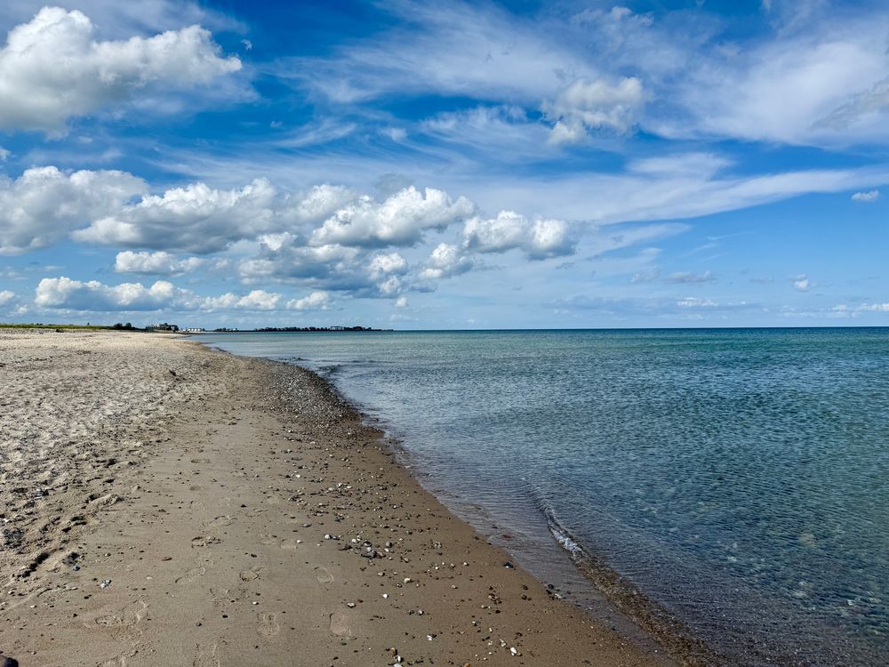 photo of a beach and the sea, there’s fluffy white clouds in the sky