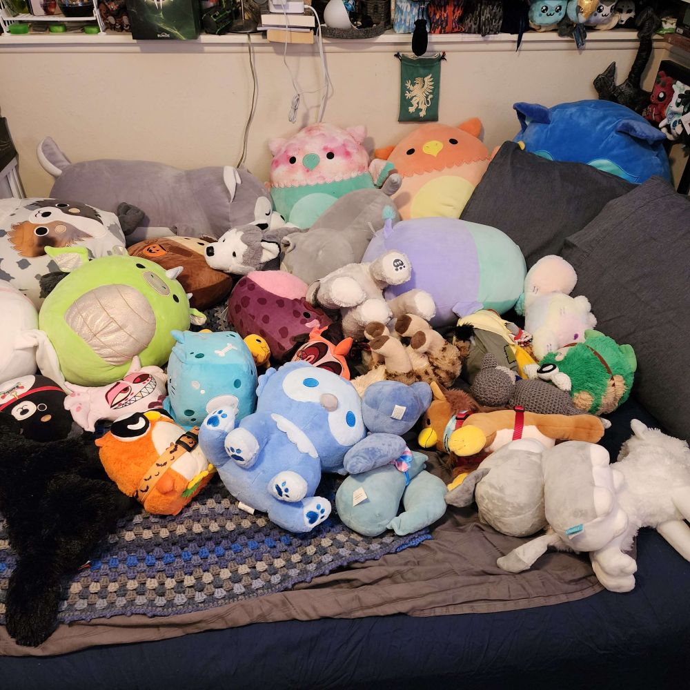 A pile of various plushies messily tossed onto a bed; there are gryphons, dragons, squishmallows, hyenas, dogs, Foxes, and wolves in a range of realistic and fantastical colors.
