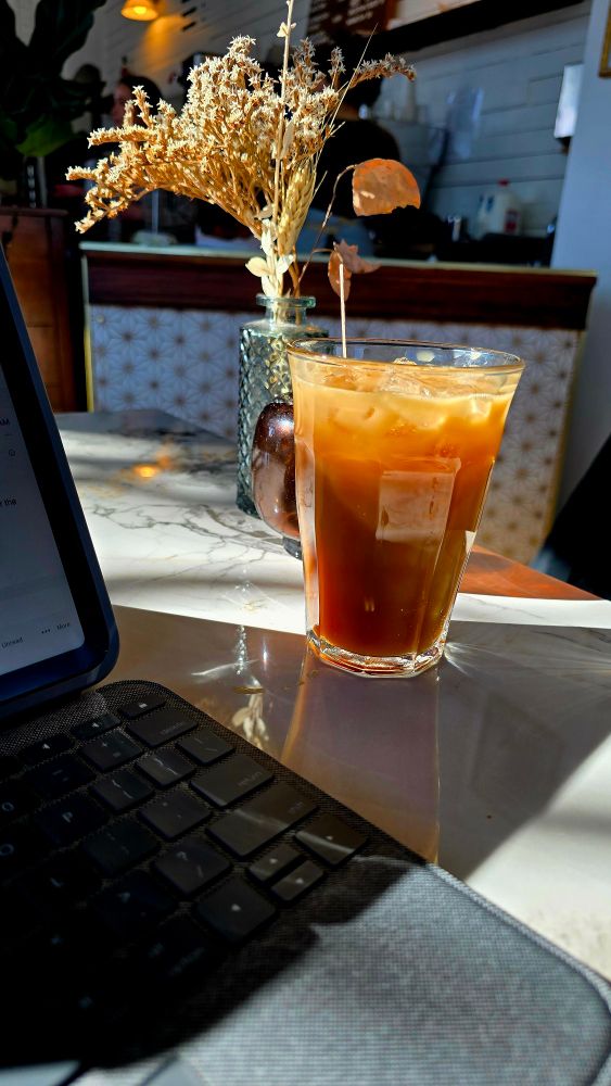 An iced coffee sits on a marble table next to dried flowers and an iPad. 