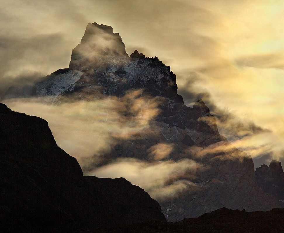 The Cuernos del Paine silhouette against a glorious morning sky, as beautiful rainbow clouds move in, hiding it all again from view. Torres del Paine National Park, Patagonia, Chile.