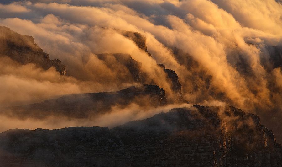 A moment of unspeakable beauty as the last light of day touches churning clouds rushing over the jagged cliff faces of South Africa's Table Mountain.