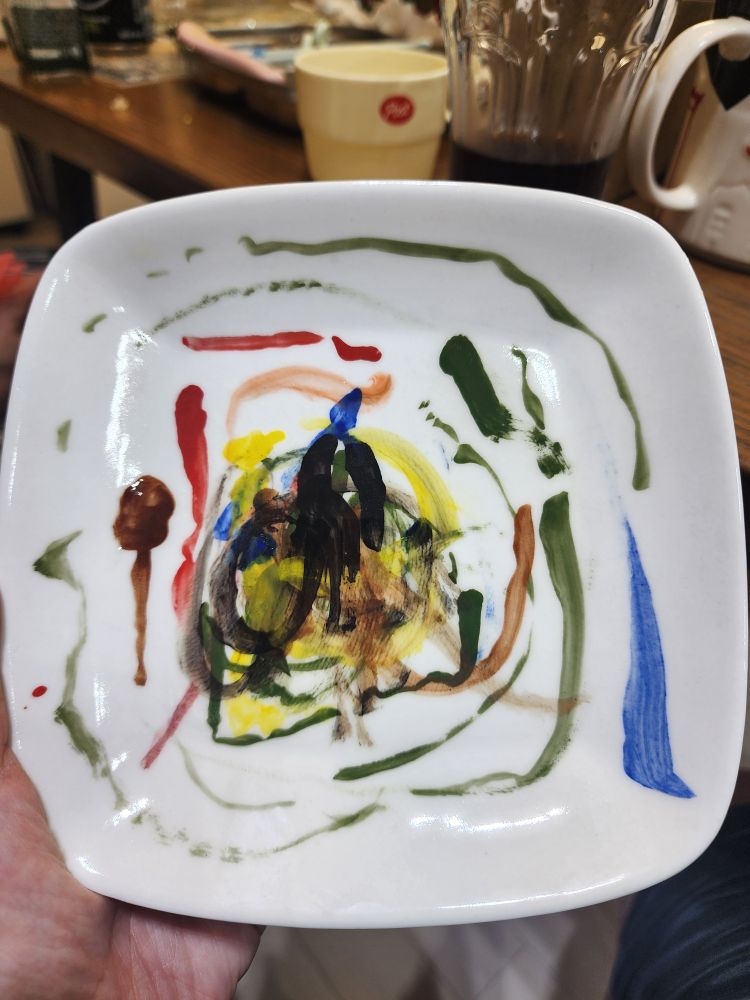 네모난 접시에 접시의 모양을 따라 삐뚤 삐뚤하게  끊어지는 선들이 빨강, 주황, 노랑, 초록, 파랑, 갈색으로 불규칙하게 그려져 있다. 접시 제일 안쪽 가운데는 검은색으로 굵은 붓질로 얼추 사람 형상이 그려져 있다.