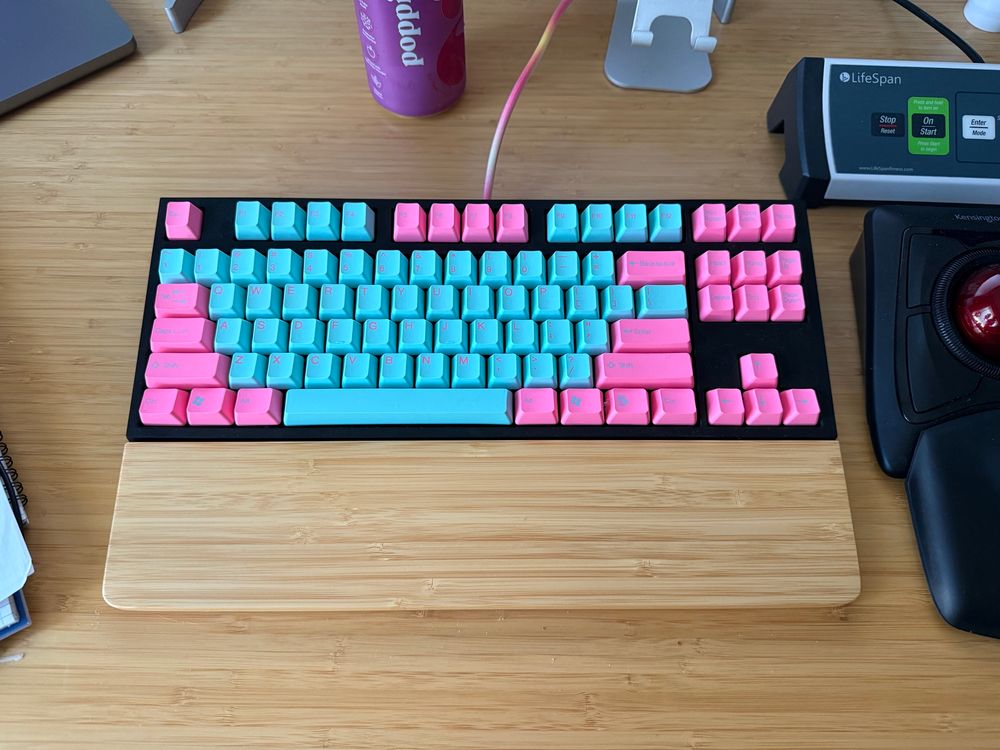 Black keyboard with neon pink and neon aqua key caps sitting on a bamboo desk.