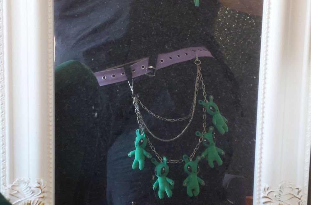 Photo of a layered silver chain attached to a belt that has five small ikea aliens attached to it.