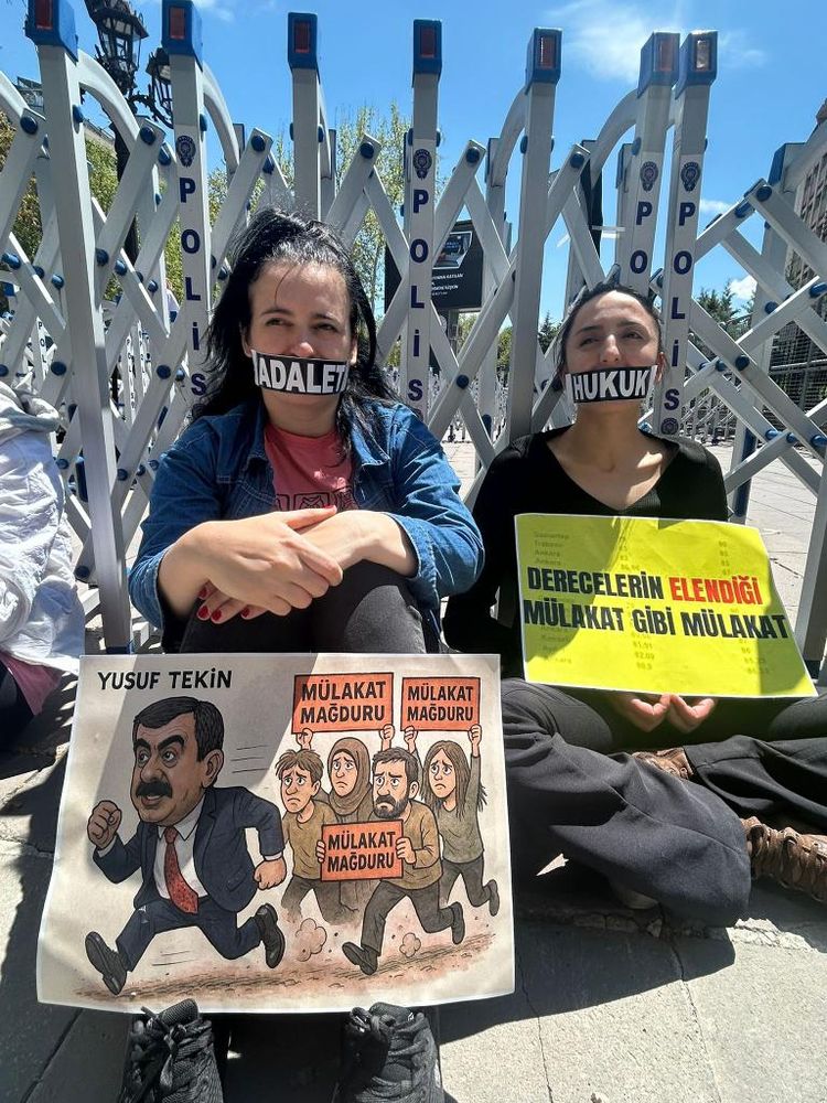 Soldakinin ağzı "adalet" sağdakinin "hukuk" bandıyla kapatılmış ili kadın oturuyor polis bariyeri olduğu anlaşılan yerin önünde. ellerinde döviz ve karşkatür döviz var