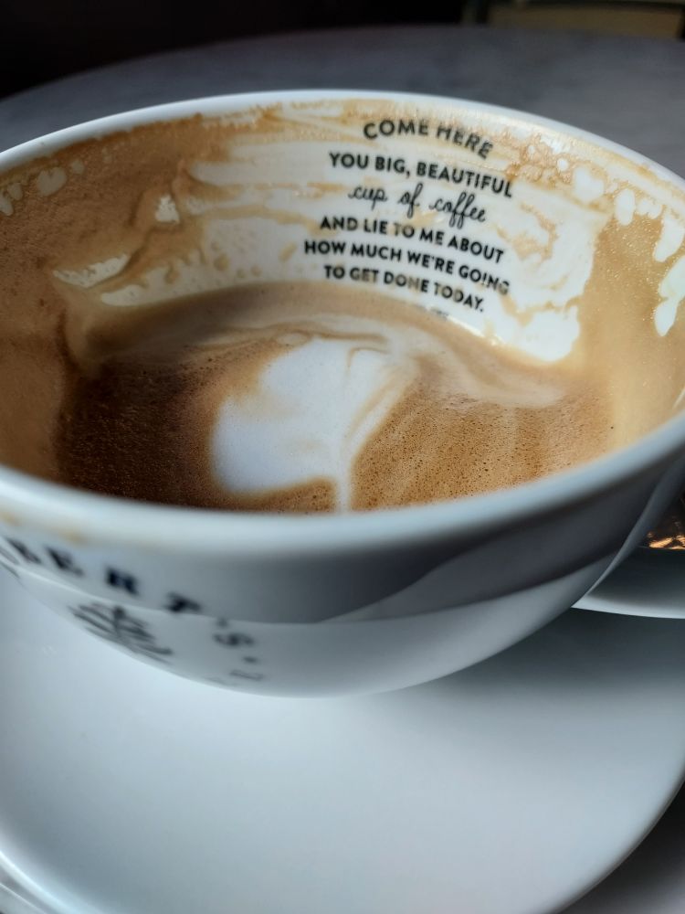 Robert's Coffeen puoliksi juotu kahvikuppi, jonka sisäpinnalla lukee "Come here you big, beautiful cup of coffee and lie to me about how much we're going to get done today"