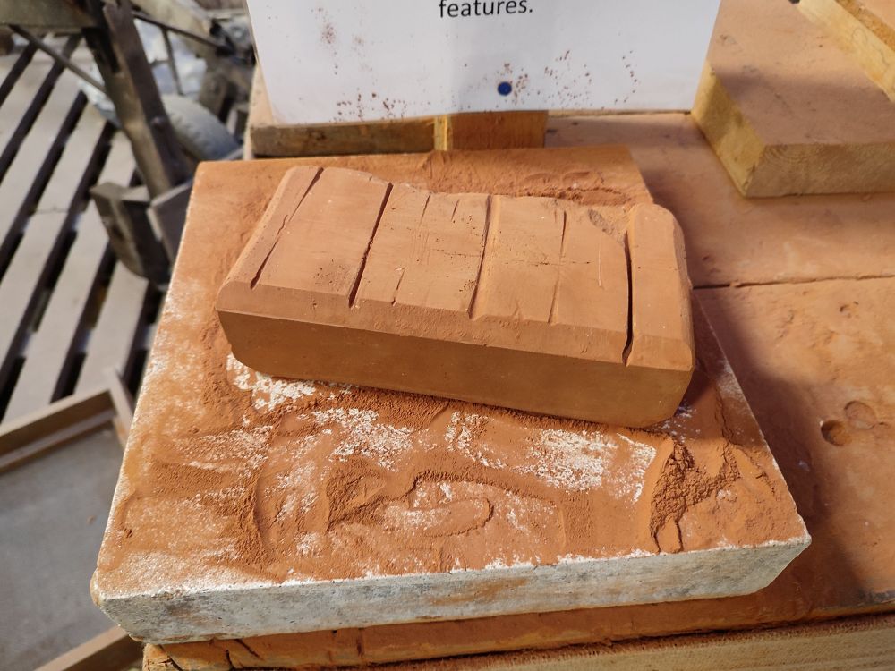 An example of a single rubbing brick on a rubbing stone, looking like a soft browny red hunk of chalk or pastel with chamfered edges