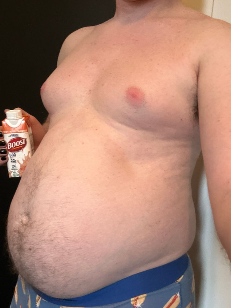 Fat man holding a Boost next to his big belly, which is hanging over the waistband of blue boxer briefs with hot dog print