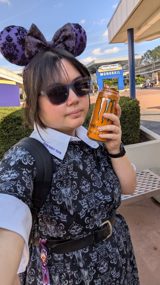 Victoria in her Haunted Mansion outfit holding an orange Monster Zero. A monorail sign is visible in the distance 