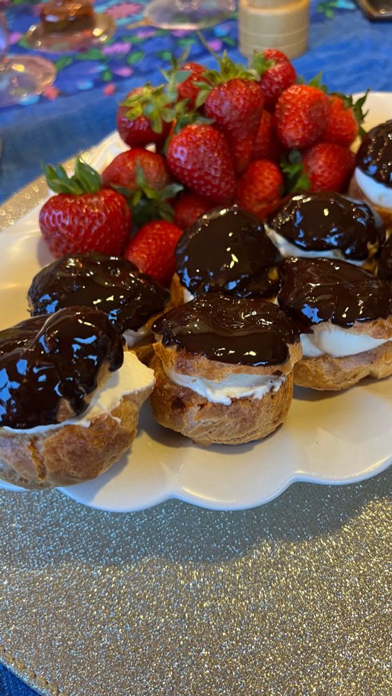A plate of profiteroles with a chocolate glaze and cream and strawberries