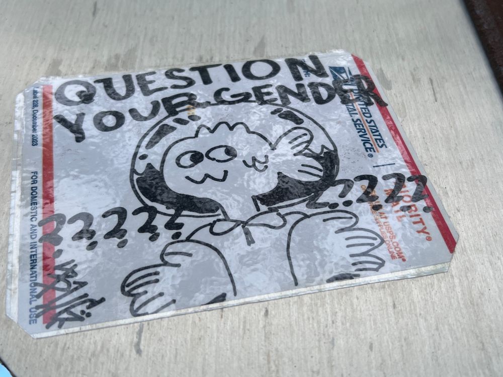 A postal label with a drawing of a fishbowl headed person surrounded by question marked that says “Question your gender.”