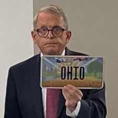 A forlorn Mike DeWine holding up a license plate that says “Ohio.”
It’s the misprint with a backwards airplane. 