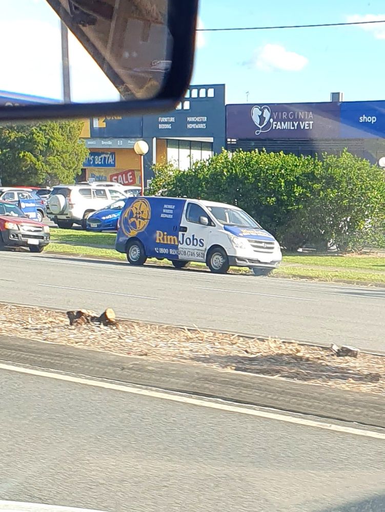 Blue and white van parked on the side of the road with yellow text  advertising a tyre repair business called Rim Jobs