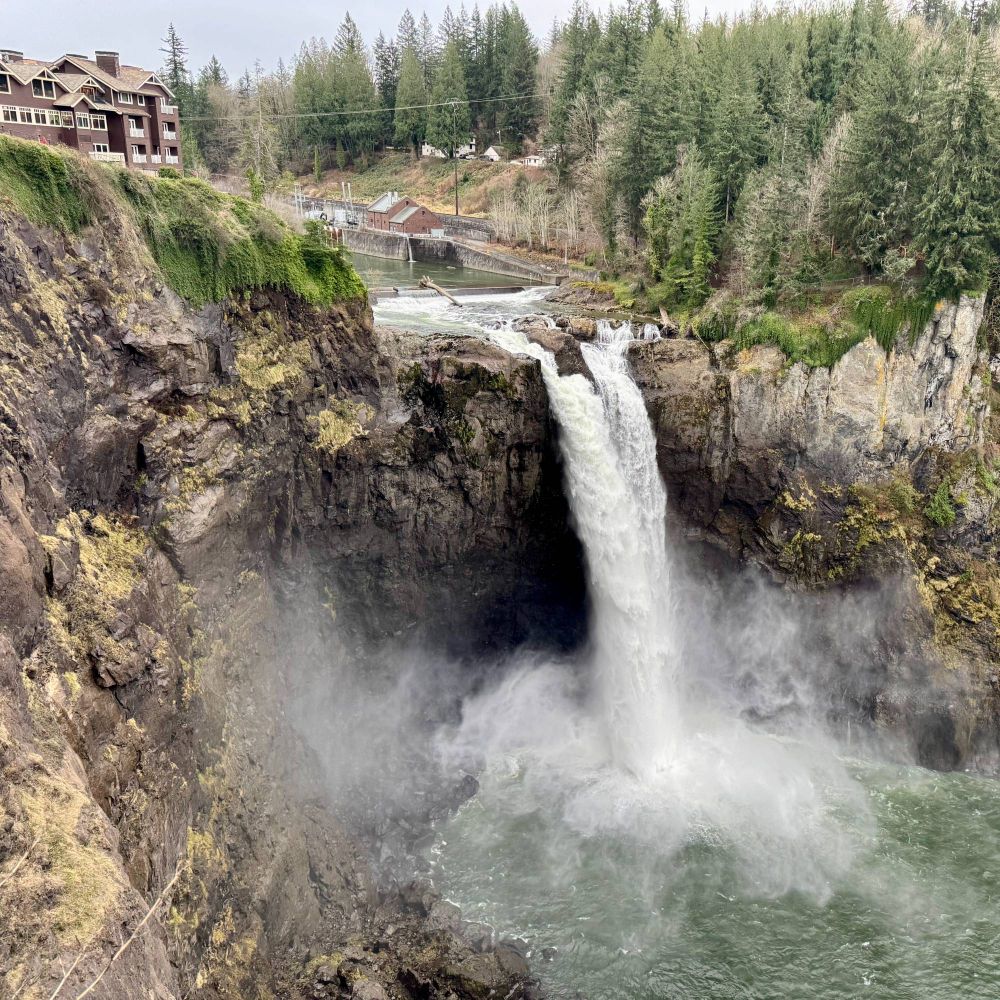 A rustic lodge perched atop a powerful 268-ft waterfall, surrounded by evergreen trees