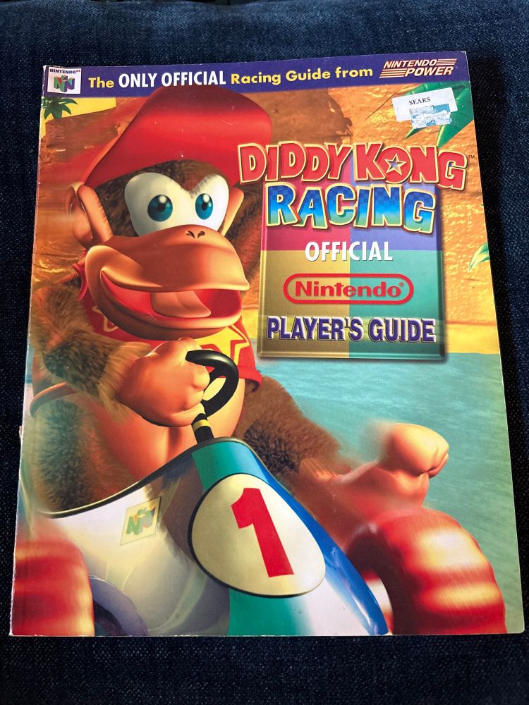 The front cover of the Diddy Kong Racing players guide, by Nintendo Power! It features Diddy with his toes FULLY out while driving at high speeds