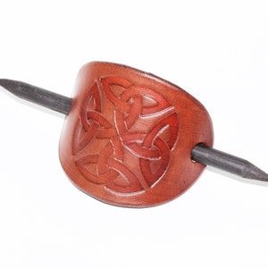 Leather hair grip with Celtic design, held up with a wooden stick. 