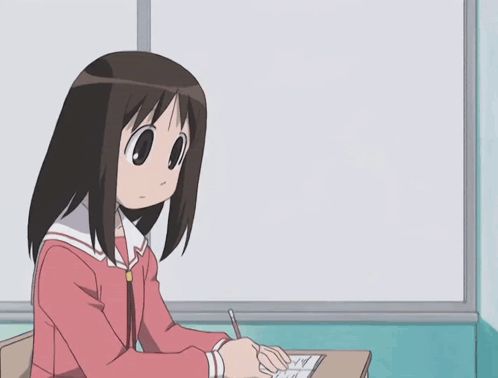 a girl sits at a desk in front of a white board with a cartoon character hanging from it