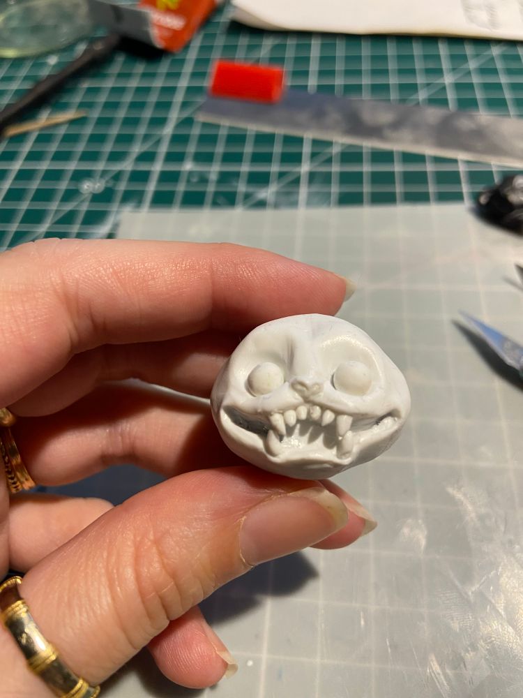 Une petite tête ronde quoique légèrement aplatie avec deux immenses orbites et des yeux tout rond ainsi qu’une large bouche aux dents pointues faisant toute la largeur du visage (fimo)