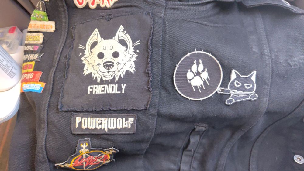 Black denim patch jacket with multiple dog/wolf/paw related patches and one black cat patch with knife in its mouth