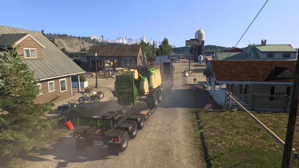 Screenshot from American Truck Simulator showing a rear view of my Kenworth K100E hauling a Krone square baler toward its destination farm, with the majestic Grand Teton Mountains towering in the background.