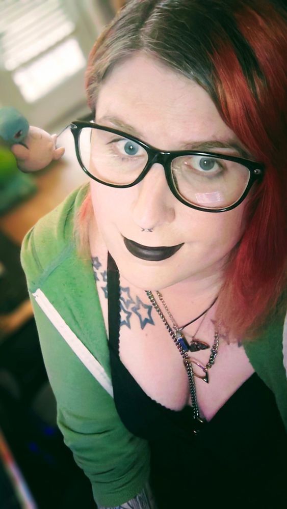 a woman with red hair, glasses, green hoodie, and a black dress