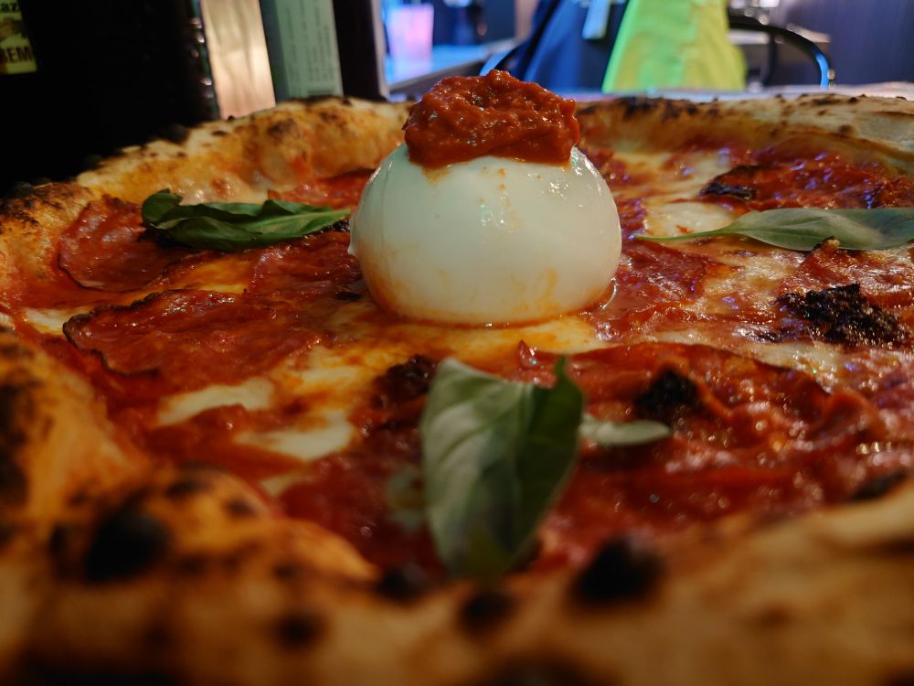 Schräg-Profilaufnahme einer Neapolitanischen Pizza, in der Mitte der Pizza liegt eine Kugel Burrata.