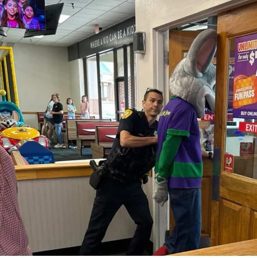 A police officer arrests Chuck E Cheese while children watch in the background 