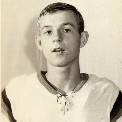 The black-and-white photo shows a young Guy Lafleur in a white Quebec Aces jersey with "AS de QUEBEC" and a four-ace logo on it. The image has a vintage border, and the background is plain.