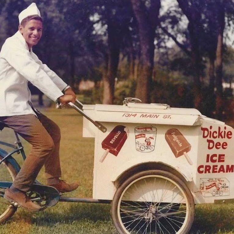 A person wearing a white uniform and cap rides a tricycle with a large 