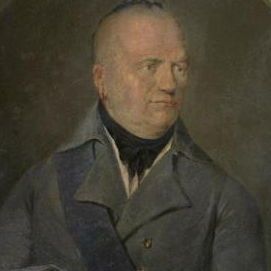 Oval oil portrait of an older European or colonial gentleman, likely from the late 18th or early 19th century. He is shown from the chest up against a dark, plain background. He wears a high-collared gray coat with two visible buttons, a white waistcoat, a black cravat, and a dark blue sash draped across his right shoulder. His hair is white and close-cropped, and his expression is stern and direct. His right hand holds a black tricorn hat against his chest. The painting shows age-related cracking and wear around the edges.