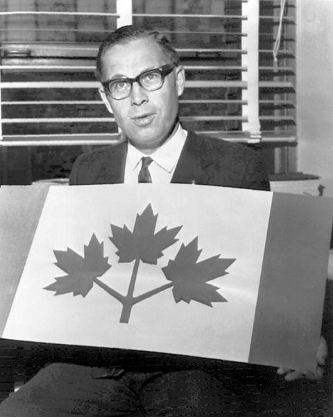 The photo is in black and white and depicts a man seated and holding a large flag design. Here are the details:

Person: The man is dressed in formal attire, wearing a suit with a tie. He is seated and appears to be presenting or showing the flag design to the camera or an audience.
Flag Design: The flag he is holding features a white field with a red maple leaf in the center, which is composed of three lobes. On either side of the white field, there are vertical red bands. This design is reminiscent of an early version of the Canadian flag, specifically the one used by Ontario from 1965 to 1975 before the adoption of the current national flag.
Background: The background includes a window with blinds or shutters, suggesting an indoor setting, possibly an office or a formal room.